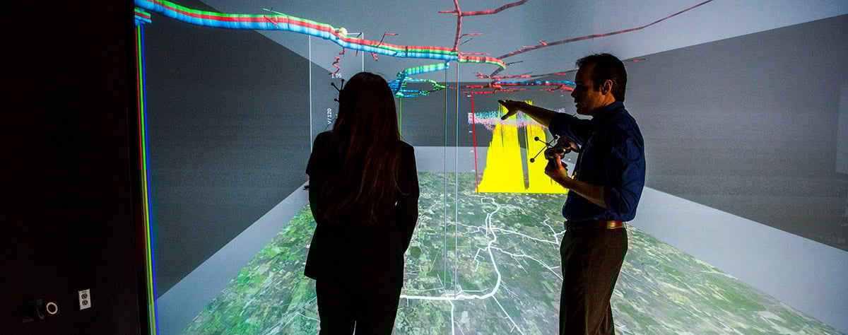 hp-energy-informatics-49722 Two people standing in front of a large, color 3D visualization screen that spans the height and width of the wall they are facing.
