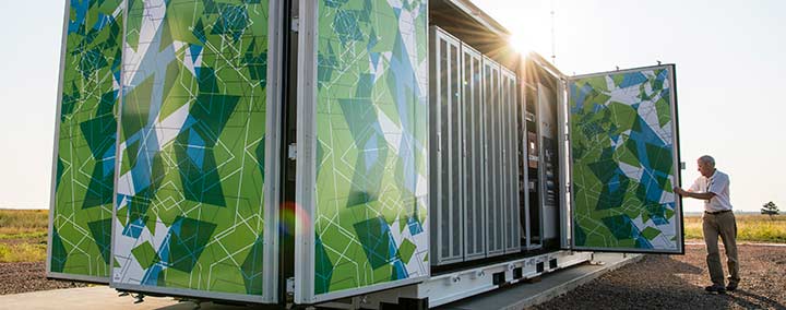 hp-energy-solutions-47219 Photo of a man closing the door of a large, multicolored metal box that is roughly the size of a semi-truck trailer. Inside the box are batteries that make up a 1-megawatt battery energy storage system.