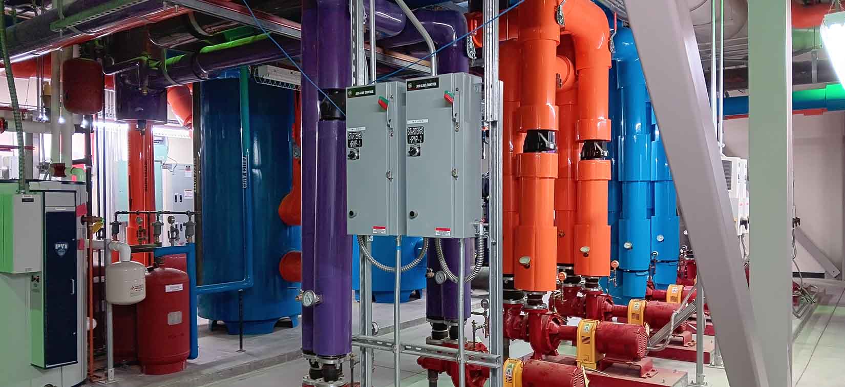Large, colorful pipes behind two circuit boxes.