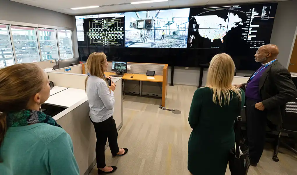 People viewing large monitors with electric grid data.