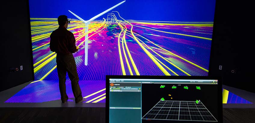 hero-about-turbineviz-26176 Photo of a researcher viewing a 3-D model of a wind turbine simulation with a computer monitor in the foreground displaying a program.