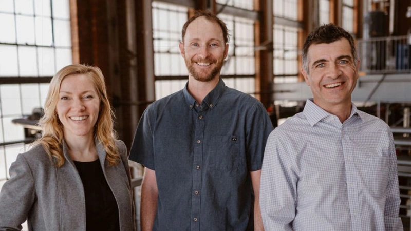 Three people in casual business dress stand together and smile for the camera.
