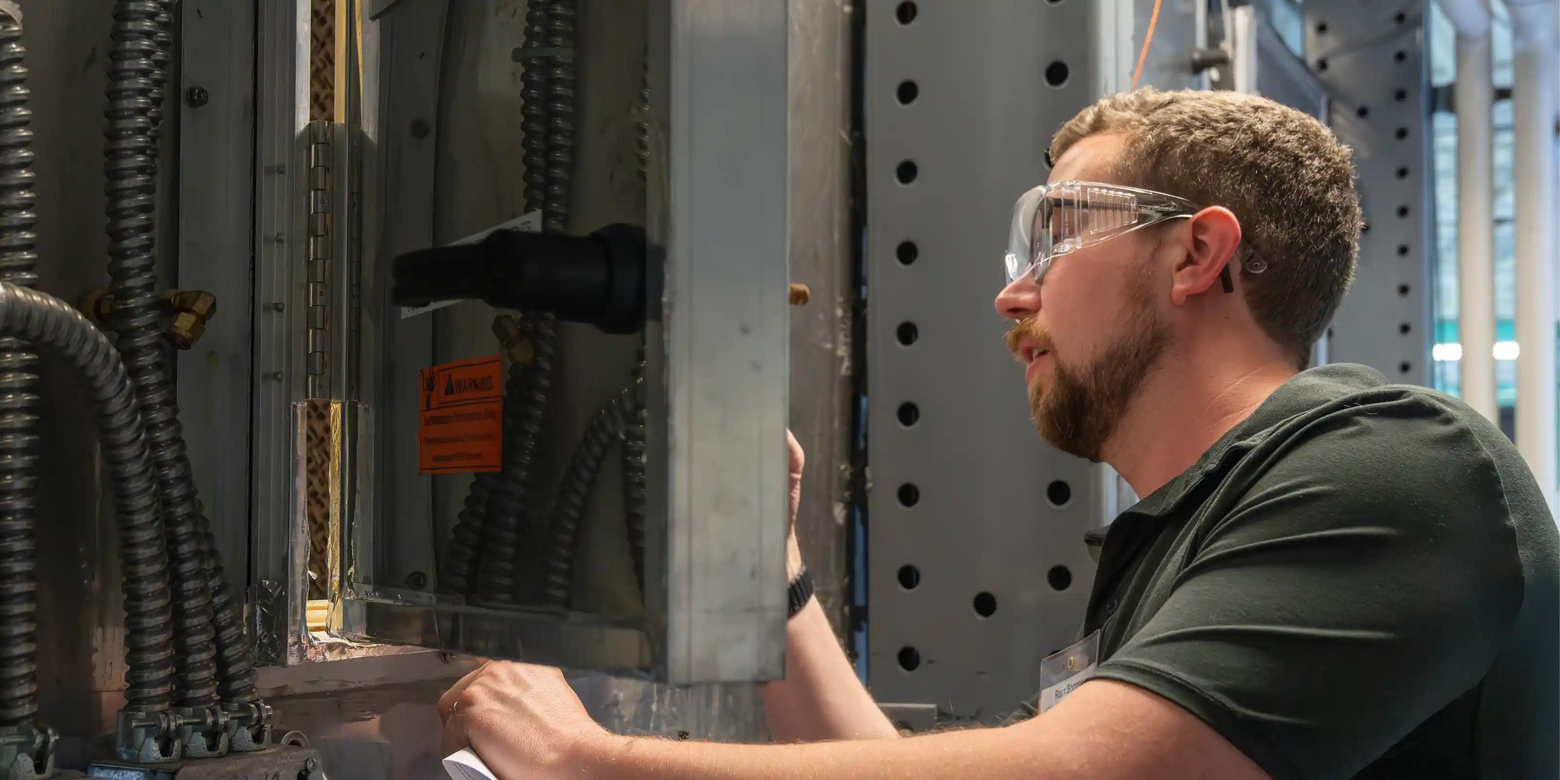 A person in safety glasses looks at a metal piece of equipment.