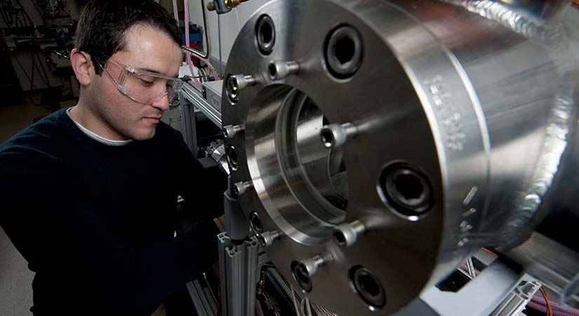 photo-thermomechanical-20026 A researcher wearing protective eyewear works on a silver piece of machinery.
