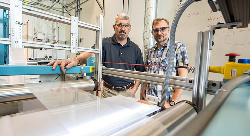 r2r-46020 Two NRELians stand with roll-to-roll equipment in a laboratory.