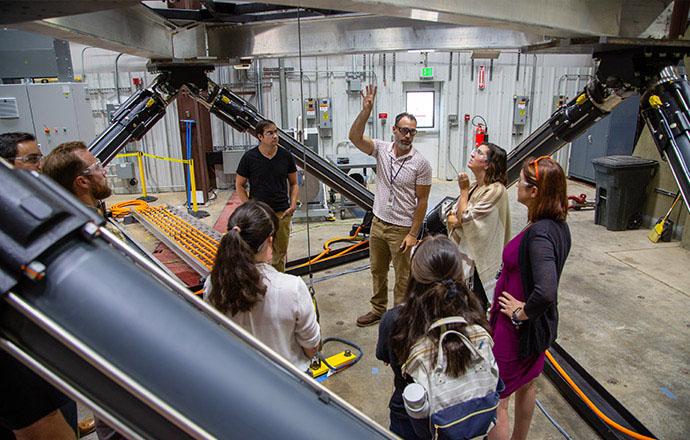 A group of people standing underneath large machinery in a research space.