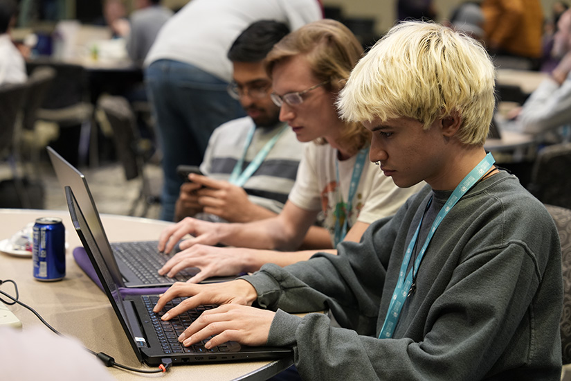 Three people wearing lanyards sitting at a table working on laptop computers.