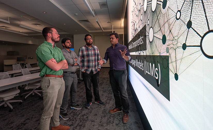 A group stands next to a large 3D screen.