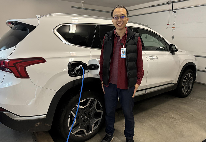 A man stands in a garage in front of an electric vehicle that is being charged.