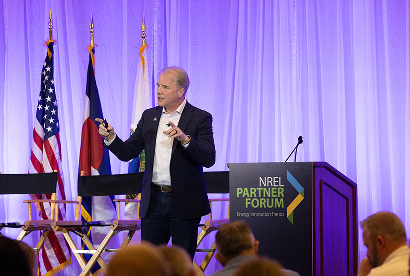 20250605-powering-data-nrel-partner-forum-puts-everything-on-table-99171 A person standing next to a podium gestures while speaking to an audience.