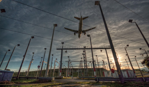 Photo of a large commercial airplane flying over electric infrastructure at an airport