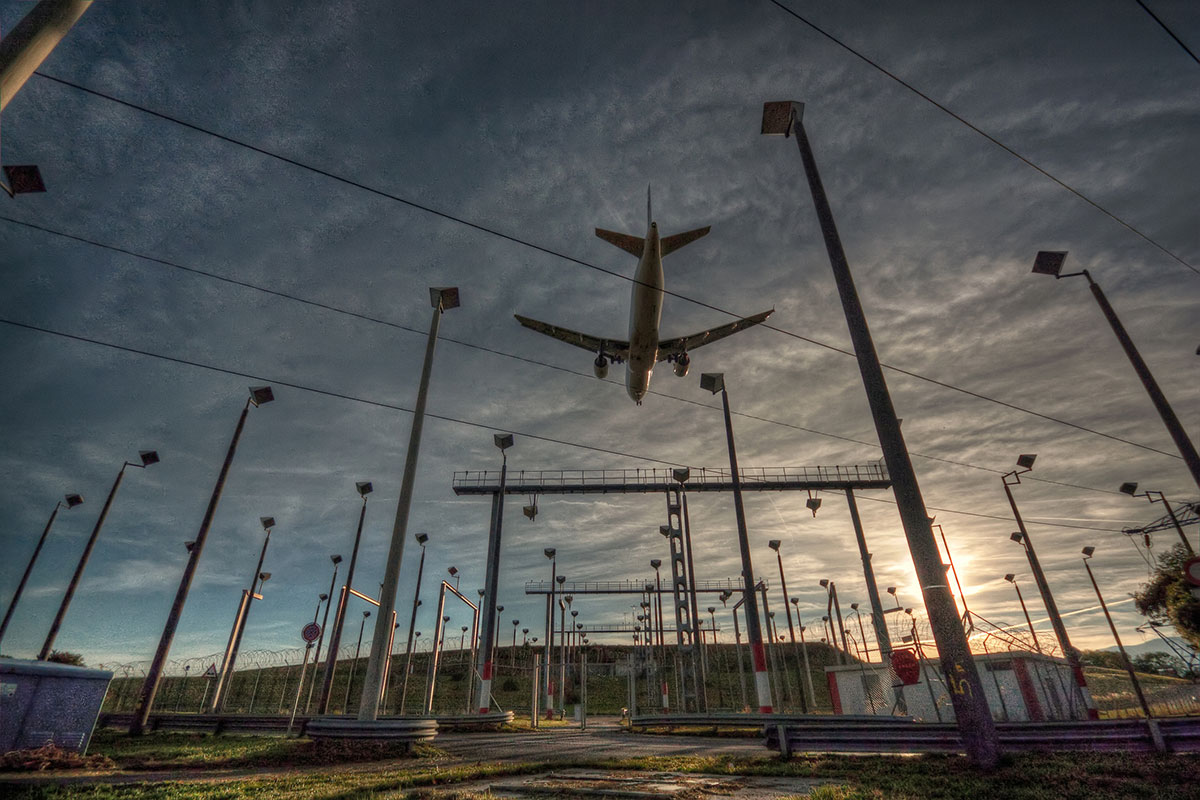 20250707-beyond-flights-airports-could-bolster-grid-security-and-adaptability-plane-gettyimages-138121492 Photo of a large commercial airplane flying over electric infrastructure at an airport
