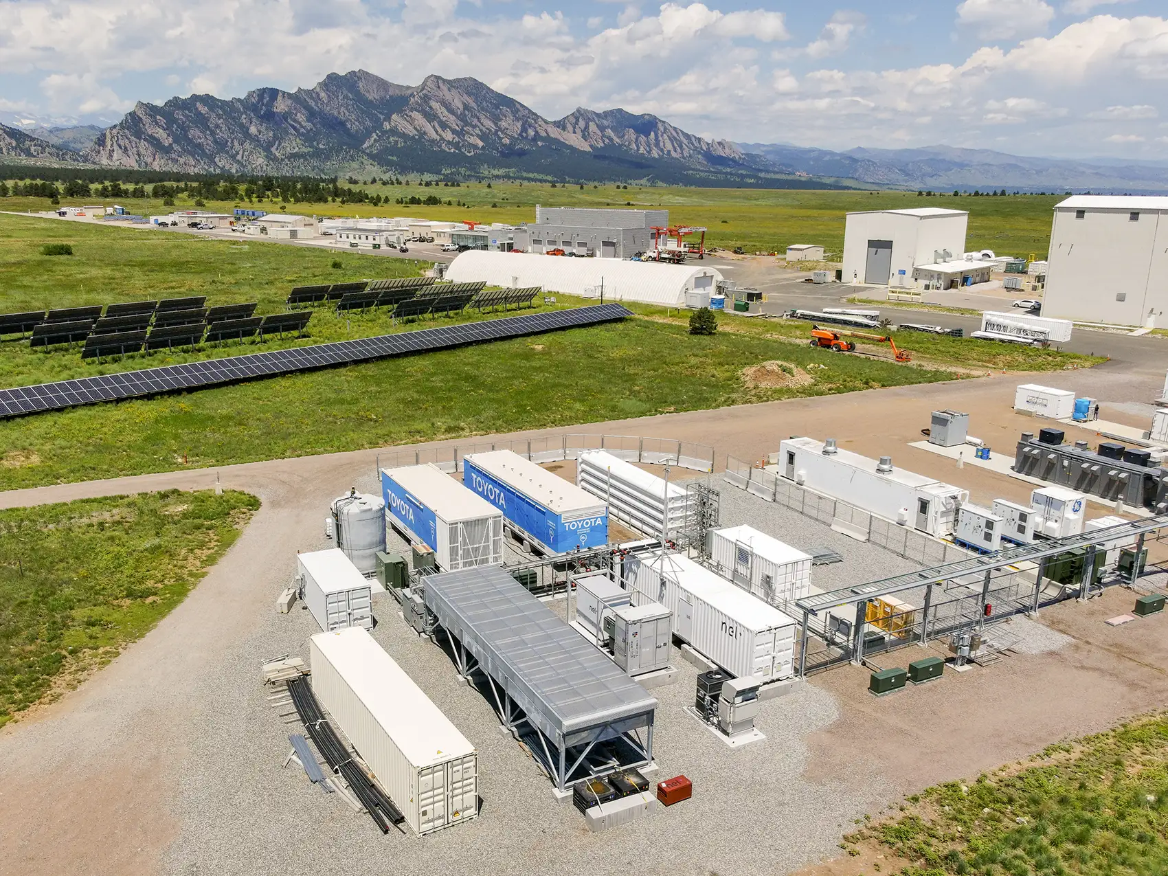 Rows of shipping containers and solar panels with mountains in the background.