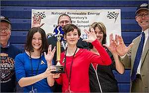 Photo of two students holding a trophy, surrounded by four adults.