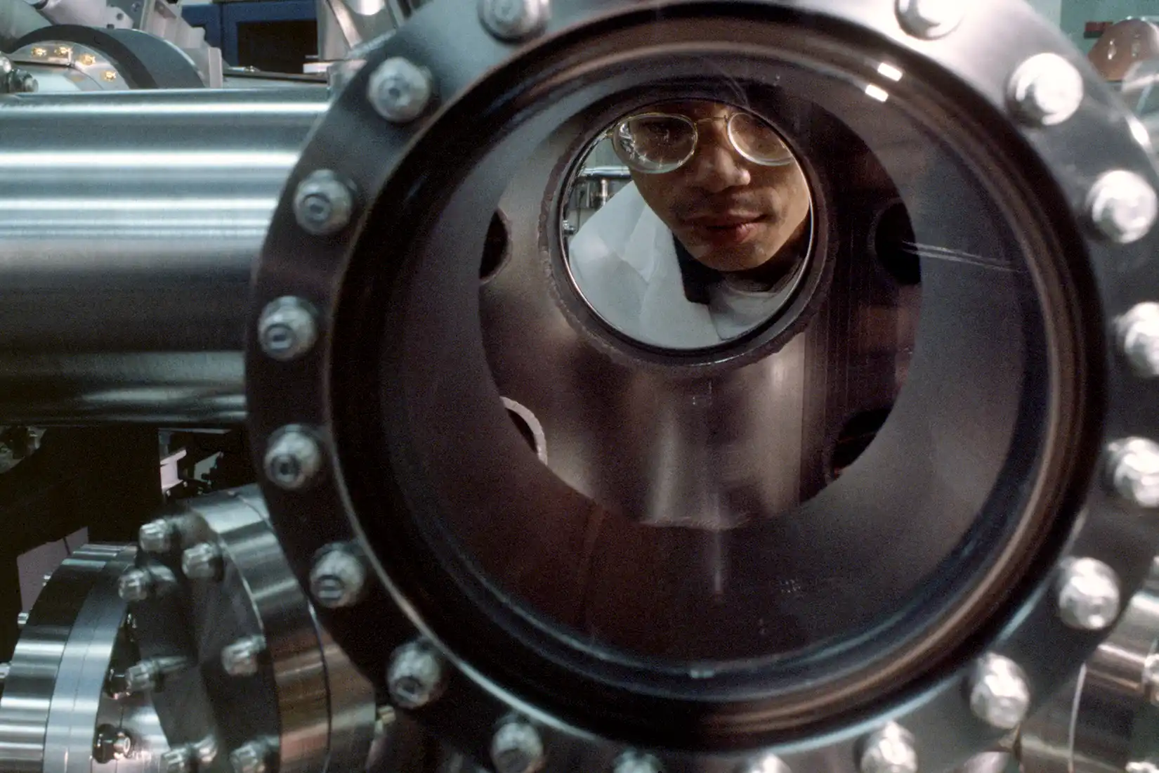 Researcher looking through a metal tube in a lab.