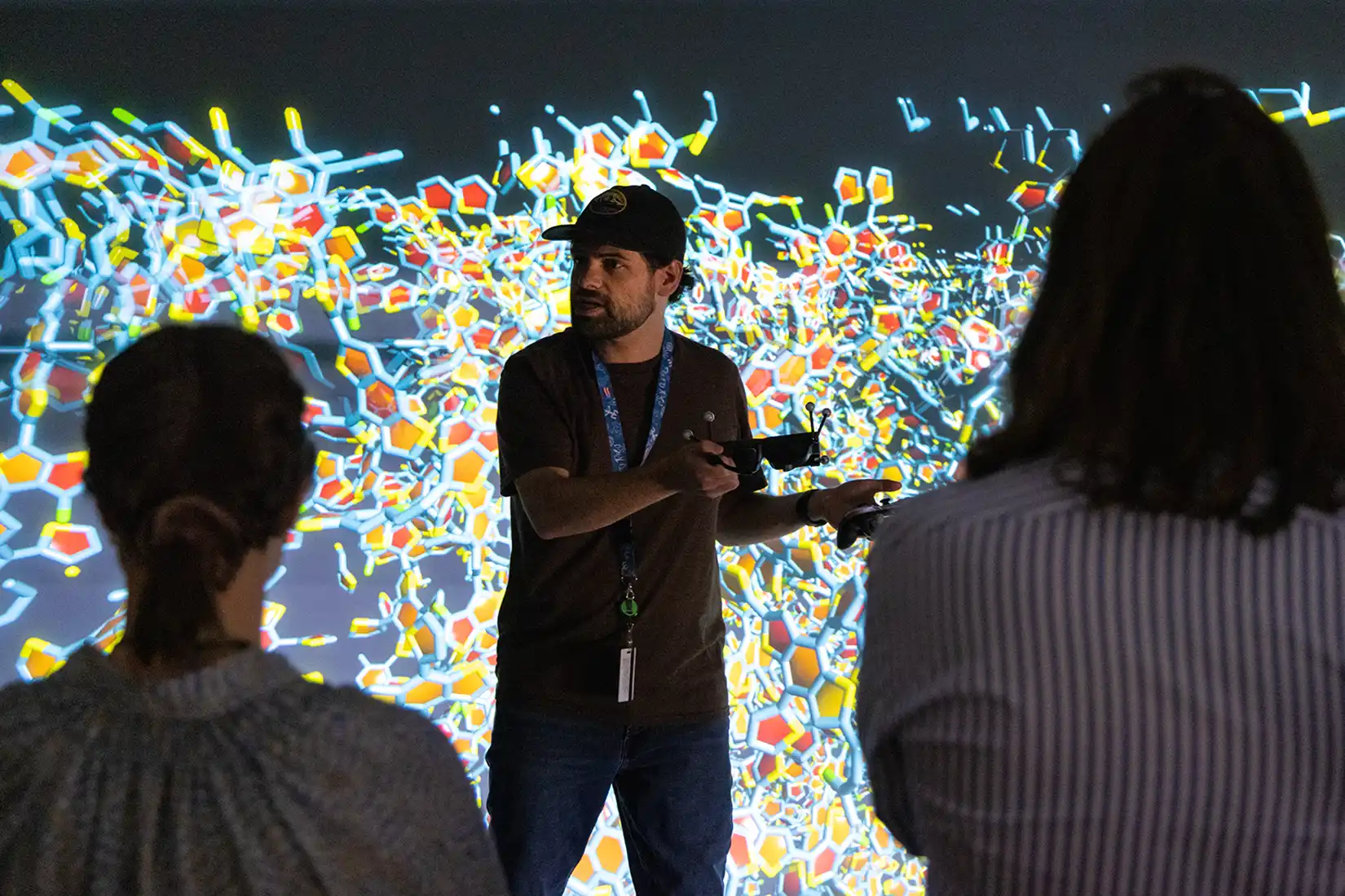 A researcher demonstrates how to use a controller to view a data visualization projected on the wall behind him.
