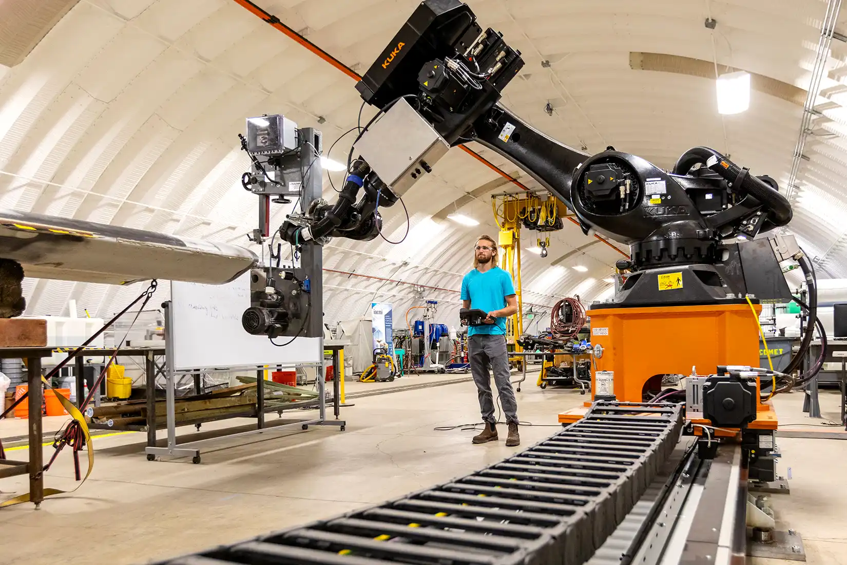 A person uses a remote control to move a robotic arm in a warehouse