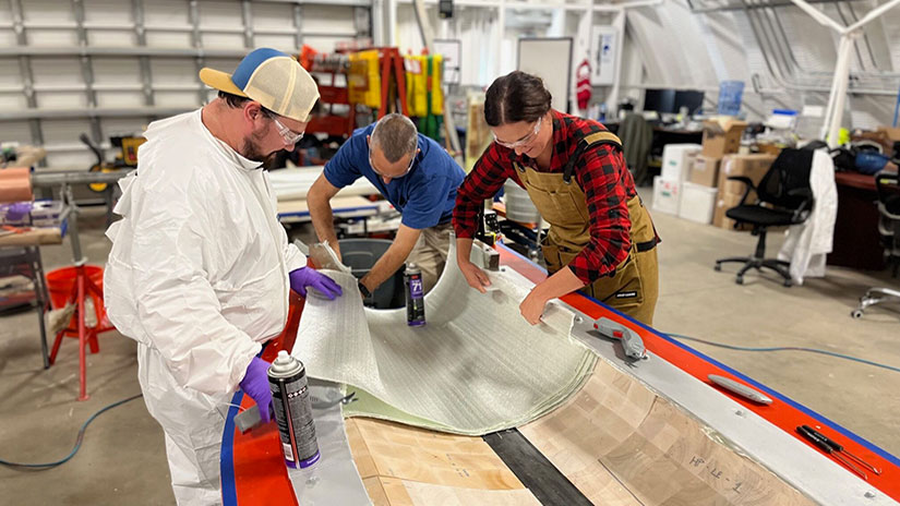 Three researchers in protective attire lay sheets of material in a mold