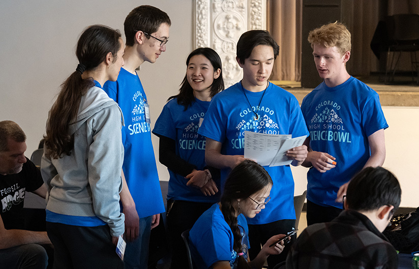 A group of students talking and looking at sheets of paper.