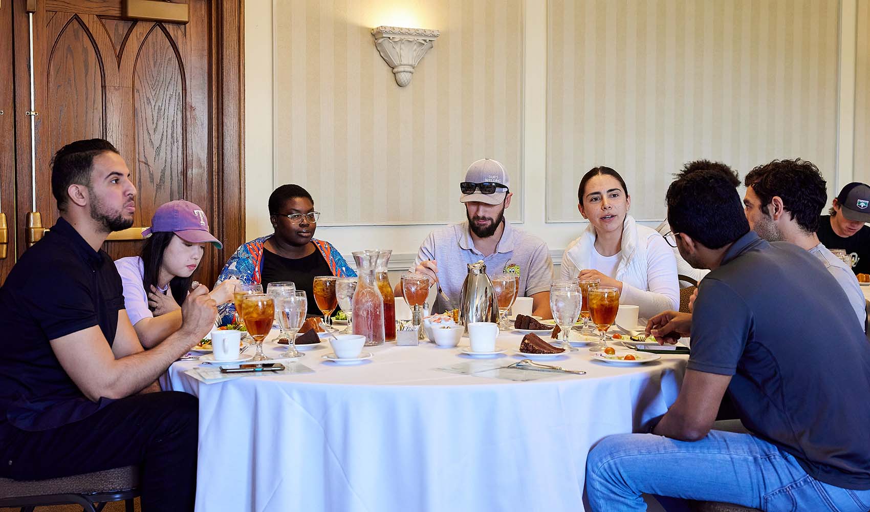 7 people sit around a circular table, eating and talking.