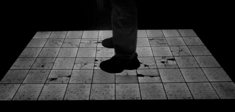 An NREL researcher stands on a PV module, cracks visible under their feet due to black and white electroluminescence imaging of the panel.