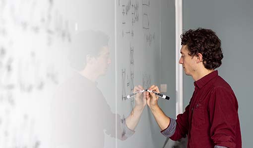 Scientist writing on a whiteboard as part of his research process into quantum computing benchmark problems