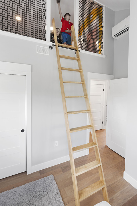 Two kids sit in a lofted area with a ladder below them.