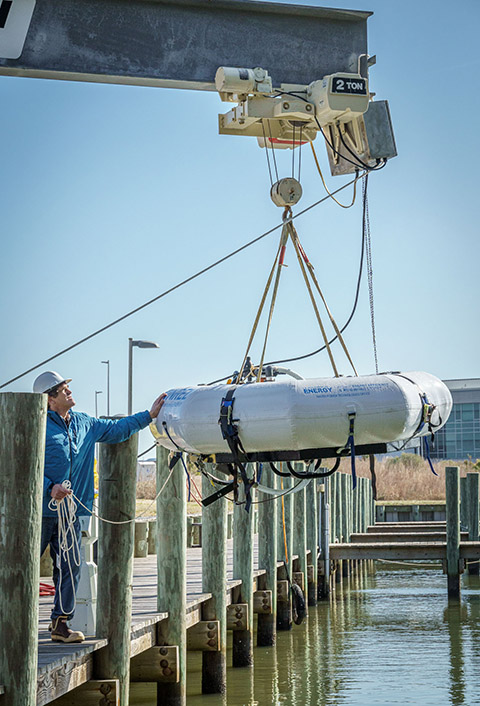 20250515-updated-risk-management-framework-supports-success-of-marine-energy-devices-73723 A machine lifts a device onto a pier.