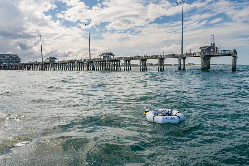 20250515-updated-risk-management-framework-supports-success-of-marine-energy-devices-hero-wec-74202 A device floating in the ocean in front of a pier.