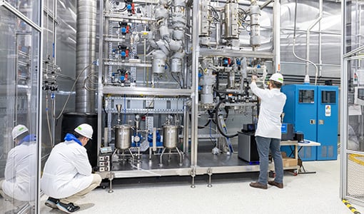 Two people in PPE work in a lab.