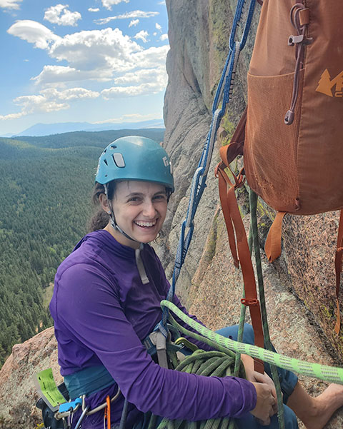 20250527-beneath-the-surface-why-bri-friedman-embraces-failure-climbing A person wearing rock climbing equipment and suspended from a rock using ropes smiles.