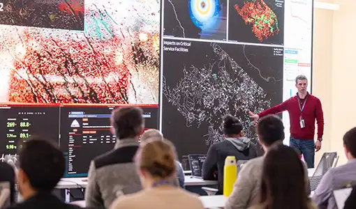 Continue reading about A person points at large screens in from of a class.