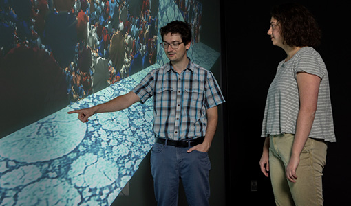 Two people examine images on a screen in a visualization lab.
