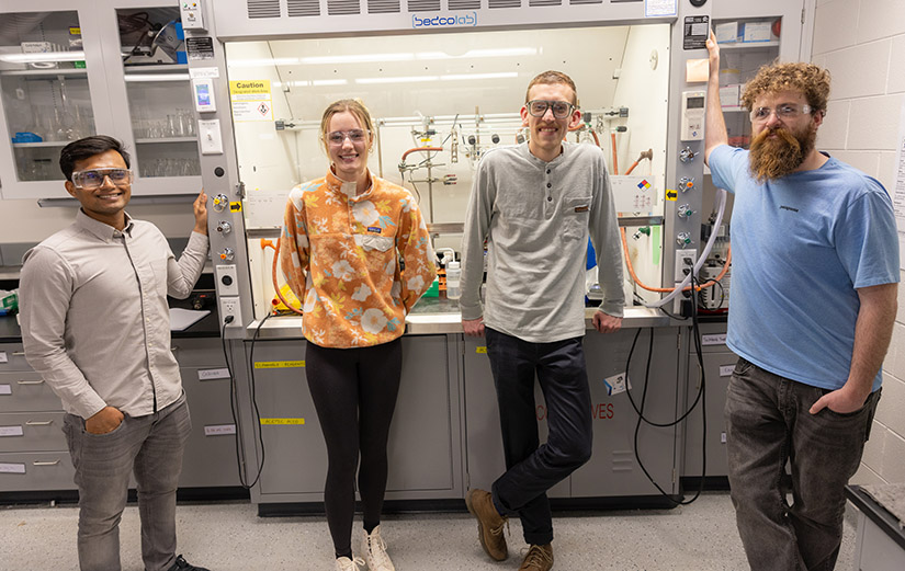 20250610-nrel-publishes-method-for-recycling-all-components-in-carbon-fiber-composites-86354 Four people stand in front of laboratory equipment.