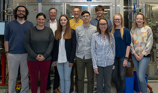 Ten people stand in front of laboratory equipment.