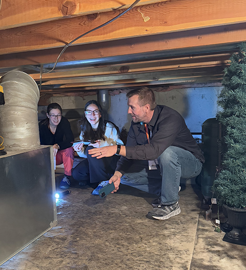 20250701-built-on-helping-others-cory-chovanec-journey-weatherization-attic Three people kneel in a crawlspace.