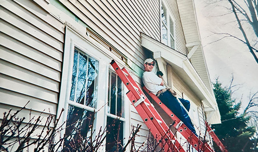 A person stands on a ladder leaning against a house.