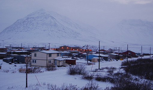 Village of Anaktuvuk Pass, Alaska, in winter, with snow-covered ground, houses, and mountains in the background.