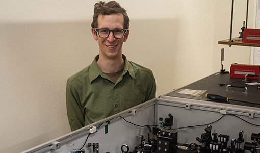 A researcher poses behind a table in a lab.