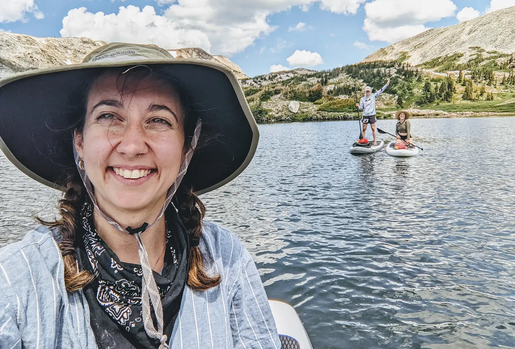 20250723-early-career-spotlight-from-astrophysics-applied-artificial-intelligence-hilary-egan-charts-creative-path-through-science-v2 A person wearing a hat takes a selfie in front of two paddleboarders on a body of water.