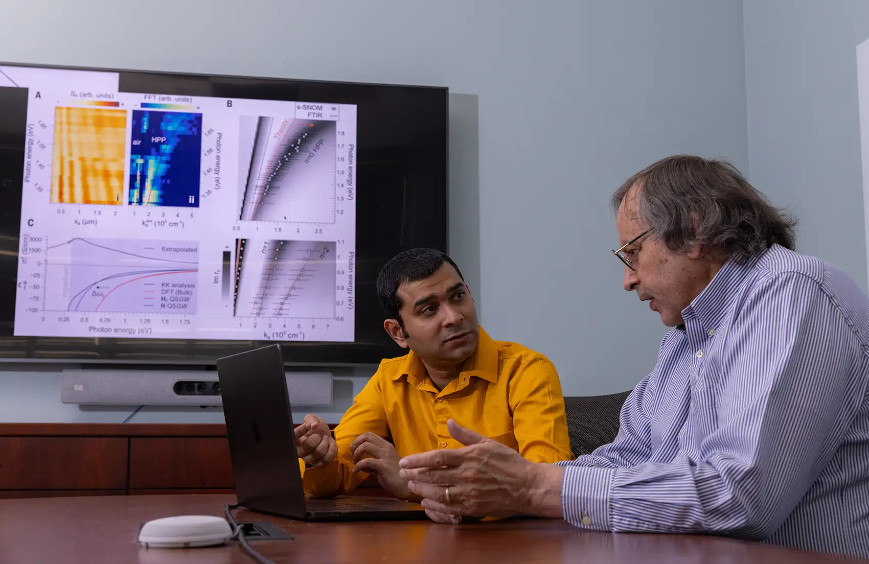 20250814-breaking-rules-but-not-waves-99398 Two NREL researchers discuss their research next to a laptop with data on a monitor screen.