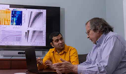 Two NREL researchers  discuss their research next to a laptop with data on a monitor screen.