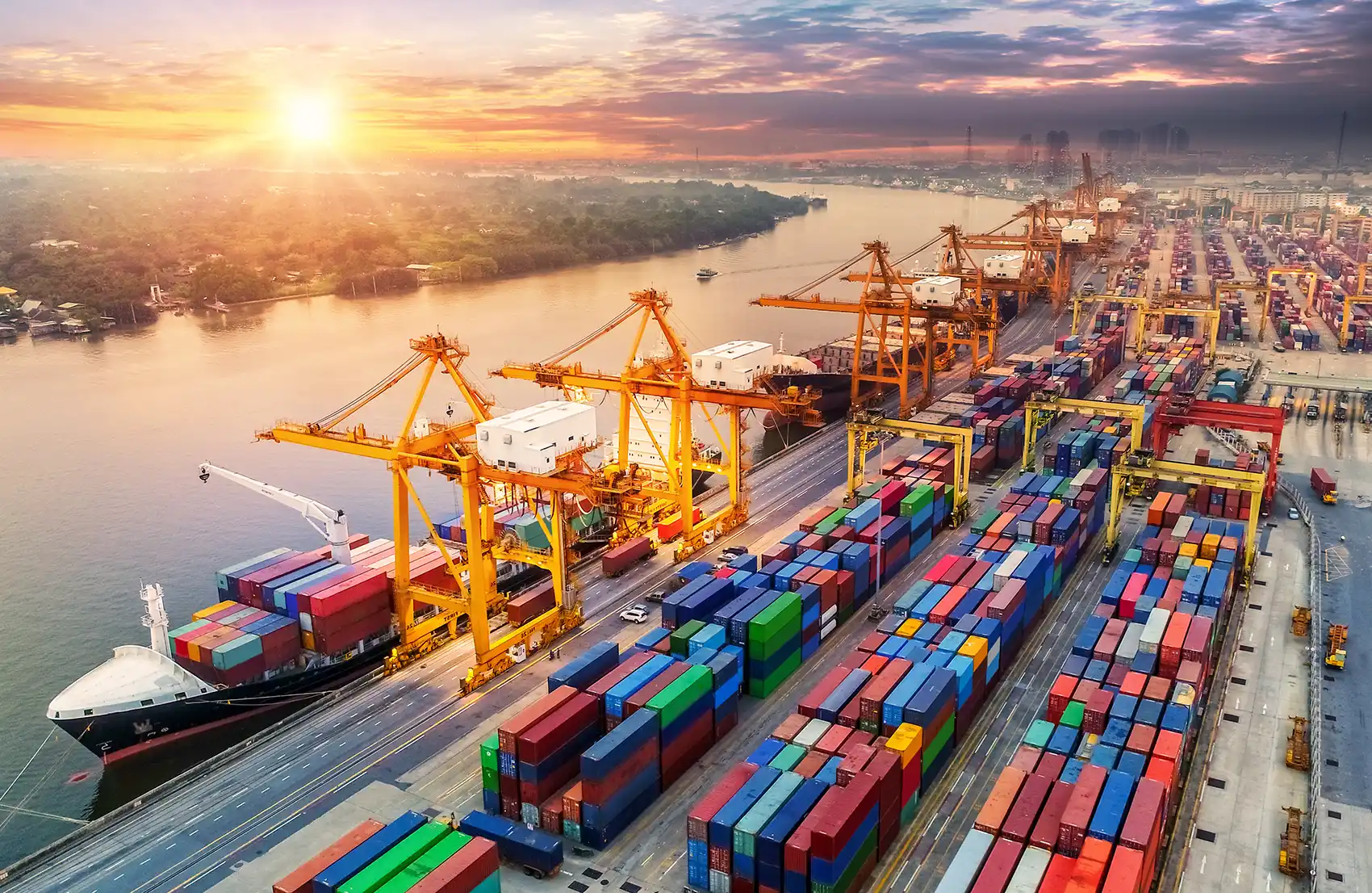 20251118-nrel-informes-tool-will-enable-streamlined-cost-effective-intermodal-freight-istock A busy port scene at sunrise. Cranes unload containers from cargo ships and stack them in colorful rows.