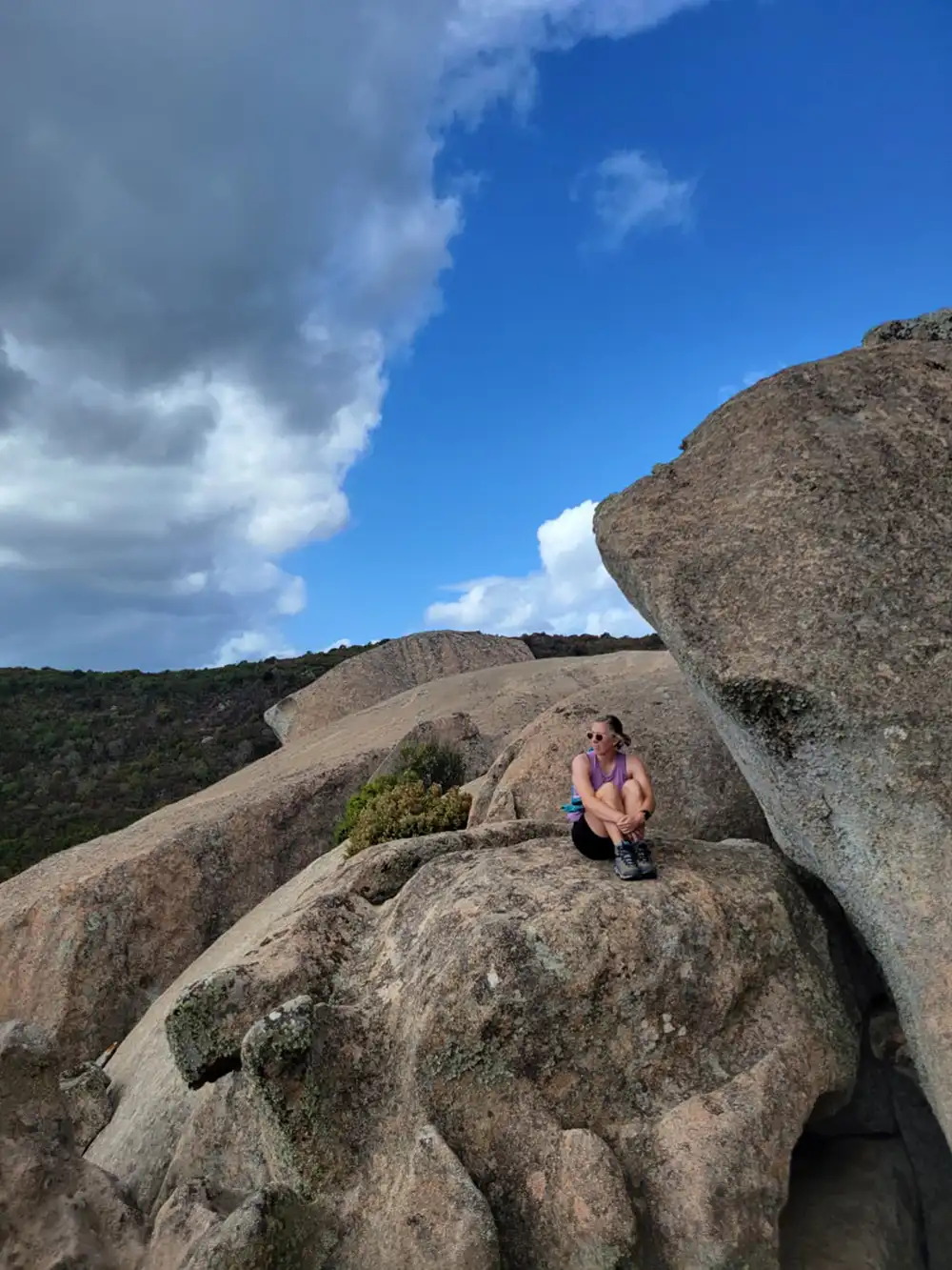 20251210-she-wanted-to-write-fantasy-now-she-is-rewriting-recycling-hiking Taylor wearing sunglasses and hiking boots while sitting on top of a large rock formation