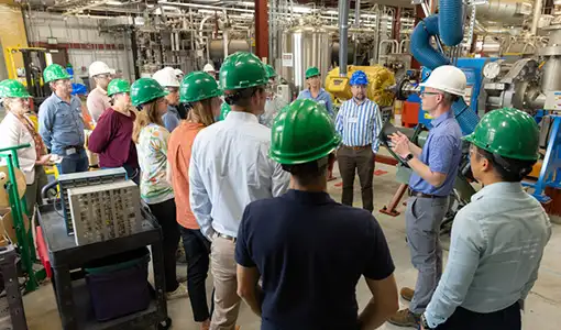 A group of people wearing hard hats stand in a lab.