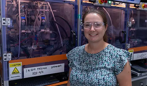 Continue reading about A woman with safety goggles stands in front of electrolyzer testing equipment.
