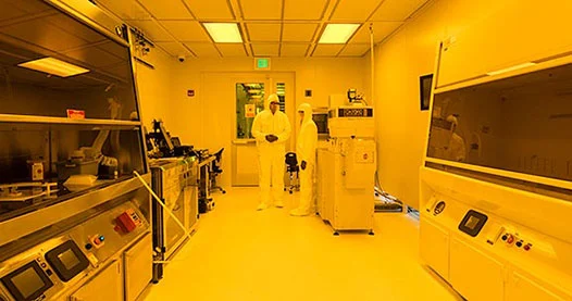 a lab with bays, equipment, and two researchers in protective gear by the door.