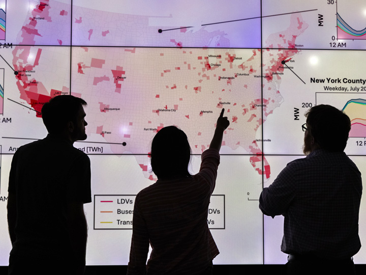 seads-89546 Silhouettes of three people pointing at a flat-screen monitor with a map of the United States.