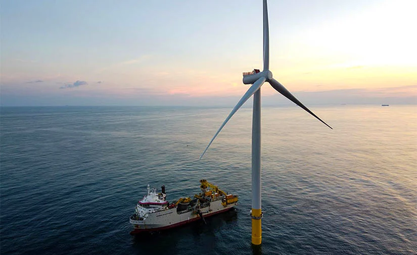 A large ship next to a wind turbine.