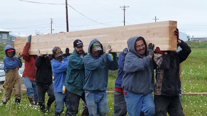 A group of people carrying a large peice of lumber.
